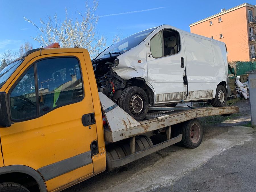 Renault Trafic blanc accidenté à l'avant, chargé sur le plateau au pied d'un immeuble